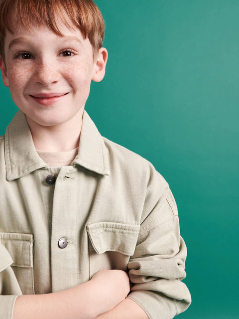 Young boy wearing a beige shirt against a teal background