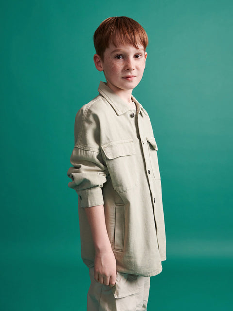 Young boy wearing a beige jacket and pants against a teal background