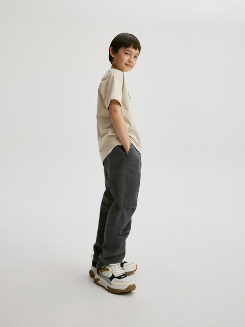 Child wearing a beige shirt and dark pants on a white background