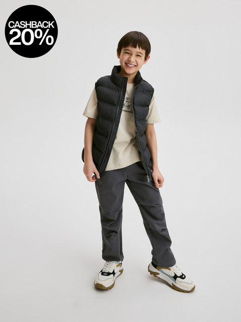 Child wearing a black puffer vest, gray pants, and white sneakers on a white background with a cashback 20% badge.