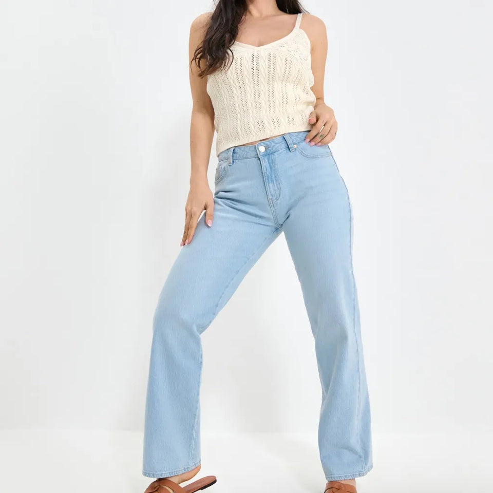 A model wearing light-wash blue wide-leg jeans and a cream-colored knit camisole top, standing against a plain white studio background.