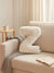 A cream-colored, plush, textured letter 'Z' pillow resting on a beige sofa in a cozy, sunlit living room setting with a gray throw blanket, a small wooden side table, and an open book.