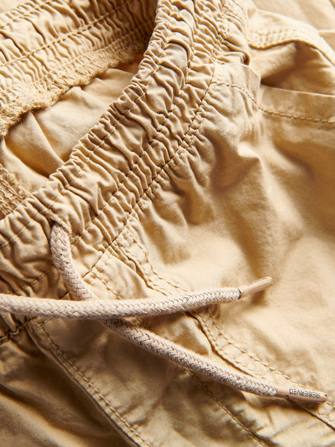 Close-up of beige pants with a drawstring, brand name visible.