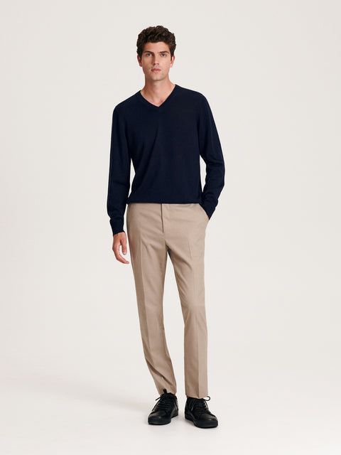 Man wearing a navy sweater and beige pants on a white background