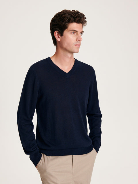 Man wearing a navy V-neck sweater and beige pants on a light background