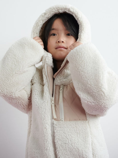 Person wearing a white fleece-lined coat with a hood on a light gray background