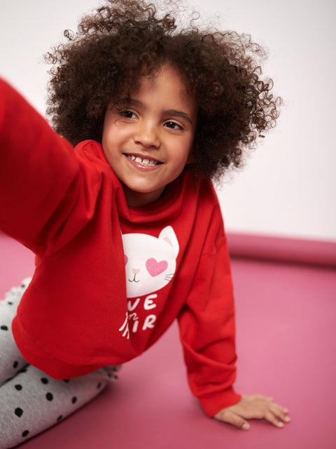 Child wearing a red hoodie with a cat design on a pink surface