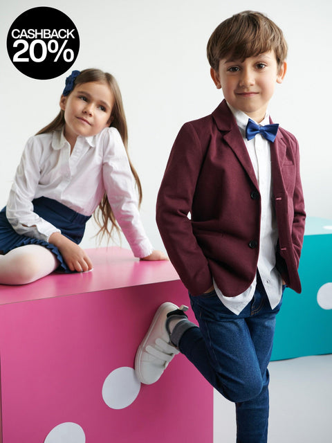 Two children in formal attire sitting on a pink surface with a white background
