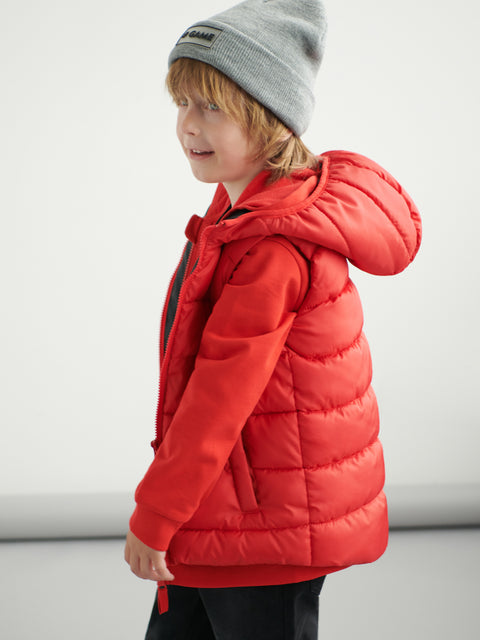 Child wearing a red puffer jacket and gray beanie on a light background