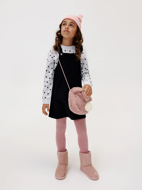 Young girl in a polka dot jacket, black dress, pink leggings, and pink boots holding a pink fluffy bag.
