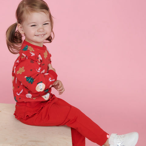 Child wearing a red outfit with Christmas-themed print on a pink background