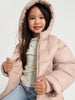 Young girl wearing a pink puffer jacket against a white background