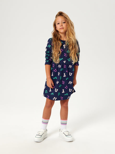 Young girl wearing a navy dress with colorful letter pattern on a white background