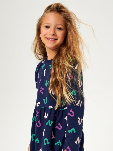 Young girl wearing a navy dress with colorful letter pattern on a white background