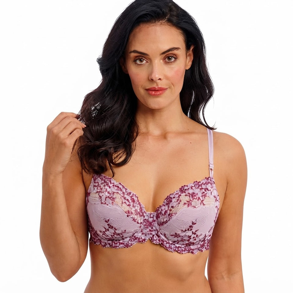 A woman modeling a lavender and purple floral lace underwire bra against a plain white background.