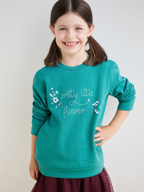 Young girl wearing a teal sweatshirt with 'pretty little flower' text and floral designs on a plain background
