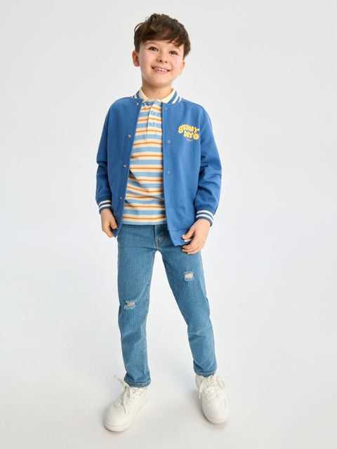 Child wearing a blue varsity jacket, striped shirt, and jeans on a white background