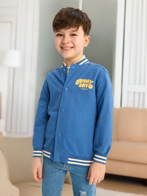 Child wearing a blue jacket with yellow text in a living room setting