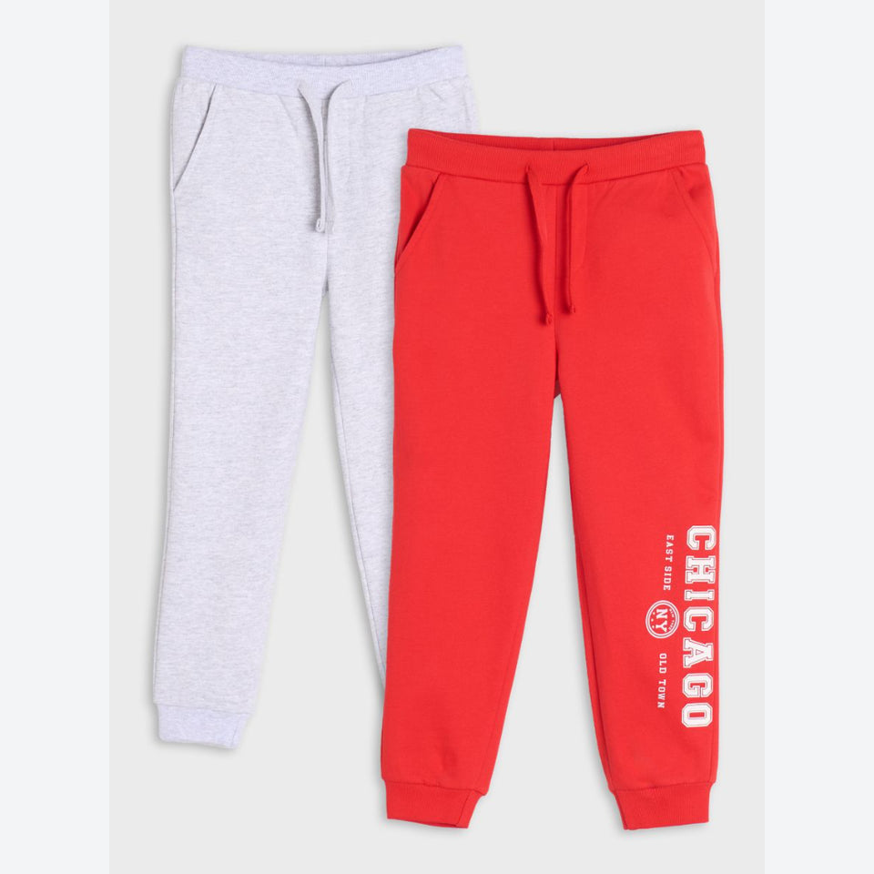 Two pairs of kids' jogger sweatpants laid flat on a light gray background. The front pair is bright red with white 'CHICAGO' text and a small circular logo on the lower leg.