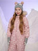 Child wearing a pink snowsuit with white star patterns and a gray hat with bear ears on a light purple background.