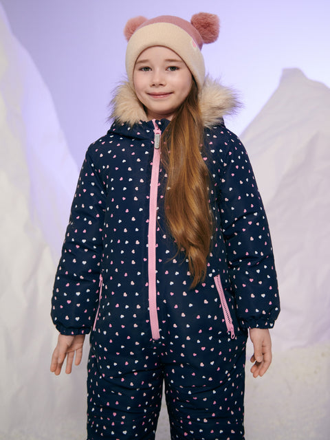Child wearing a navy blue snowsuit with pink heart patterns and a matching hat on a light gray background