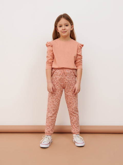 Young girl wearing a pink outfit with ruffled sleeves and floral pants on a plain background