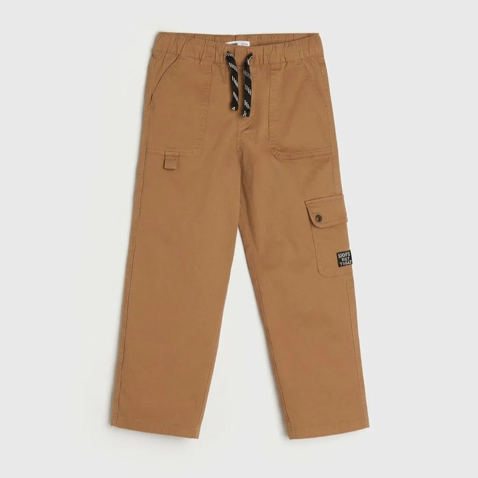 A pair of kids' cargo pants in a warm tan or camel color, featuring an elastic waistband with a black and white striped drawstring, side cargo pockets, and a small brand patch on the lower right leg.