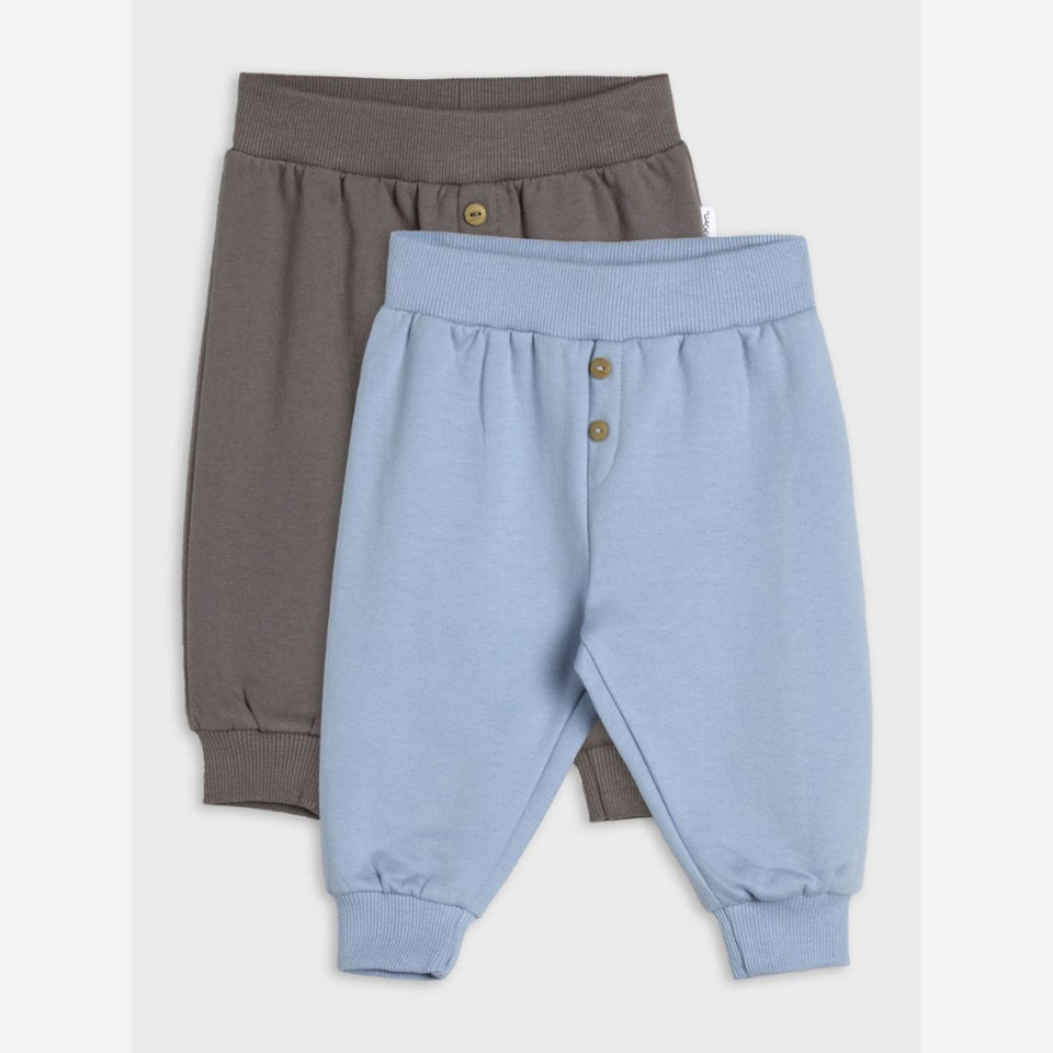 Two pairs of children's jogger pants, one in dusty blue and one in taupe brown, displayed in a flat-lay arrangement on a light gray background.