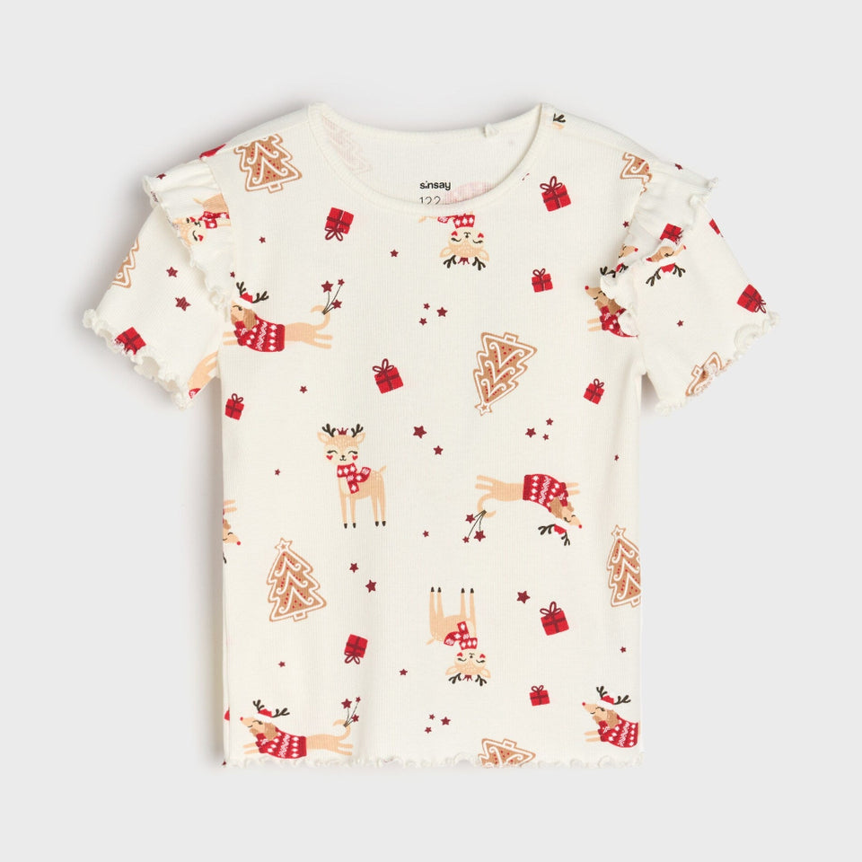 A short-sleeve baby tee with ruffled edges, featuring an all-over Christmas print of reindeer, gingerbread trees, and red gift boxes on a warm cream background.