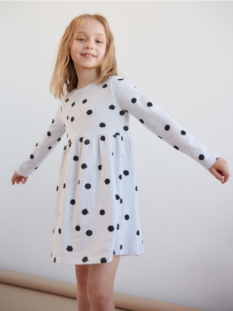 Young girl wearing a white dress with black polka dots against a plain background