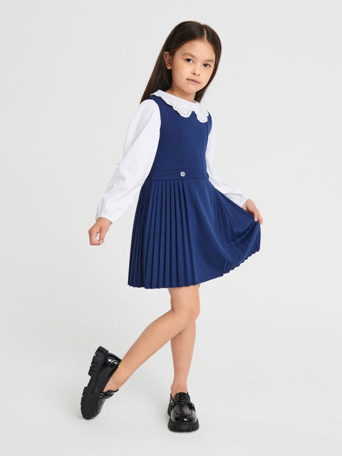 Young girl wearing a blue pleated dress over a white shirt on a light gray background