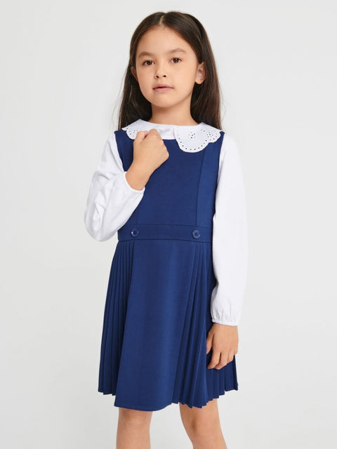 Girl wearing a blue pleated dress over a white shirt with a lace collar on a light gray background