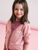 Young girl wearing a pink sweater with a heart and paw print design on a pink background