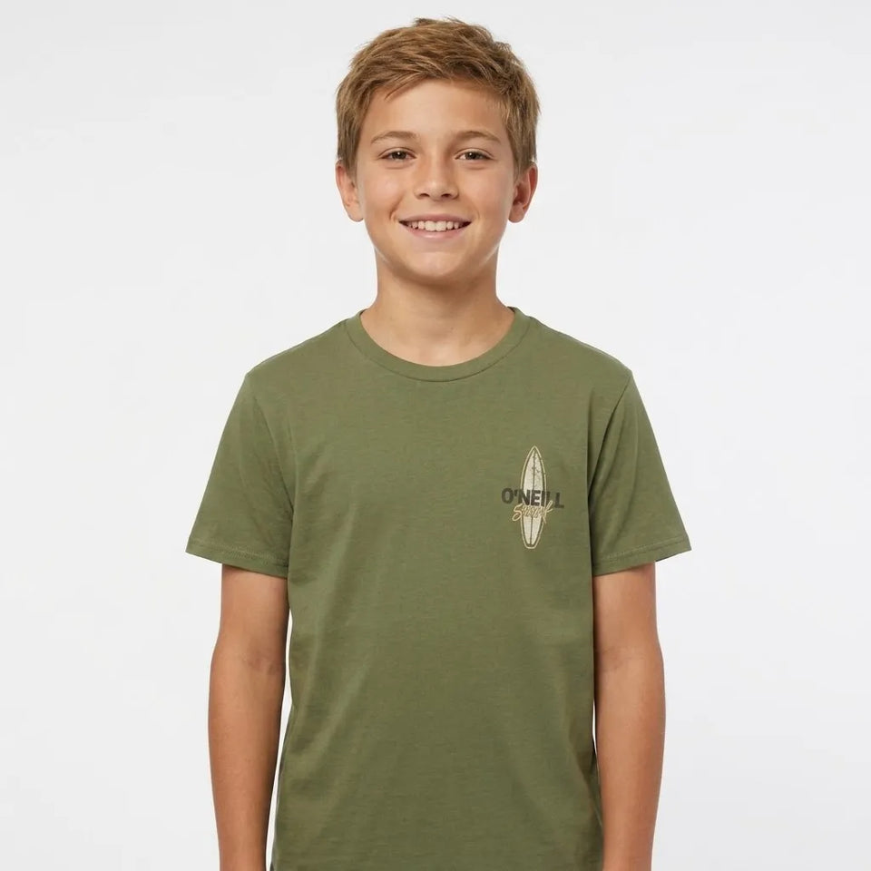 A smiling young boy with short blond hair wearing an olive green crewneck t-shirt with a small beige graphic on the left chest, photographed against a solid light gray background.