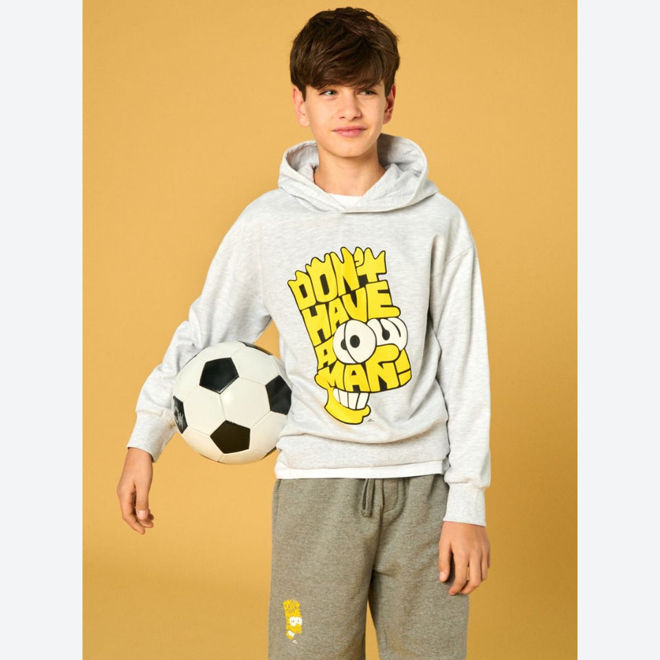 A young boy modeling a light gray heather hoodie with a yellow and black 'DON'T HAVE TO MAN!' cartoon graphic, paired with gray sweatpants and holding a soccer ball against a solid mustard yellow background.