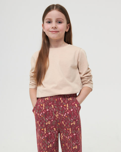 Young girl wearing a beige sweater and patterned pants on a white background