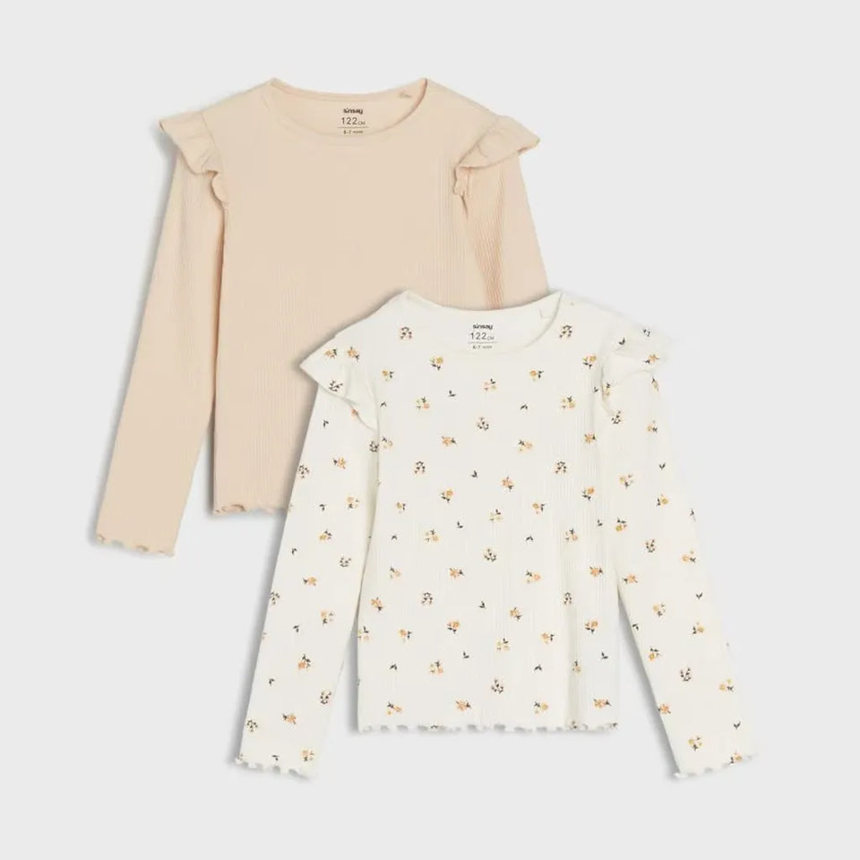 Two long-sleeve girls' tops by UGG, displayed as a set on a light gray background. The top on the left is a solid light beige with ruffled shoulders.