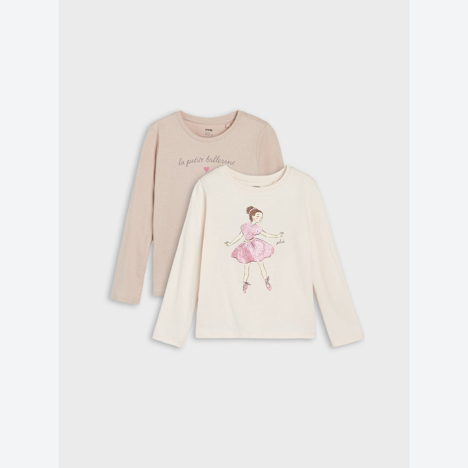 Two long-sleeve children's shirts in soft neutral tones, shown overlapping on a light gray background. The back shirt is a pale blush-beige with cursive script text, and the front shirt is off-white with a pink ballerina illustration and small text.