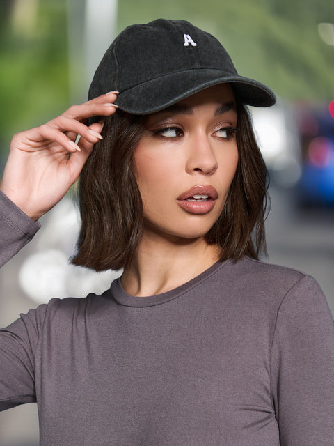 Woman wearing a black cap with a white logo, adjusting it on her head.