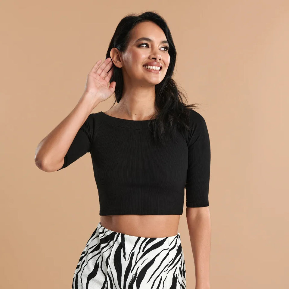 A woman wearing a black short-sleeve ribbed crop top and black-and-white zebra print pants, posing against a solid beige background.