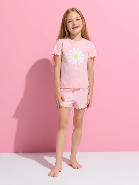 Young girl wearing a pink outfit with a white flower design against a pink background