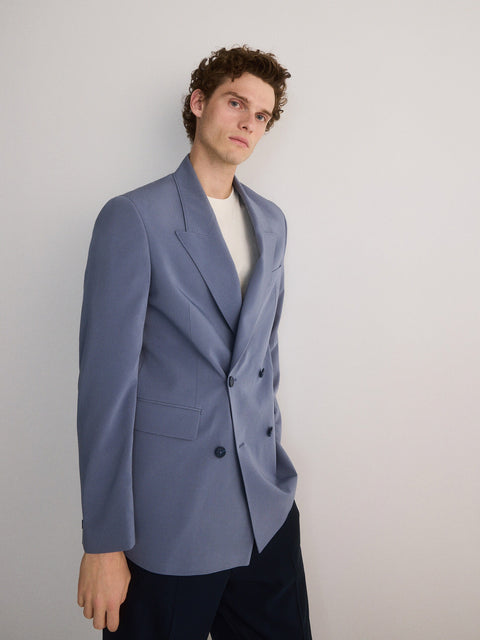 Man wearing a light blue blazer over a white shirt on a plain background
