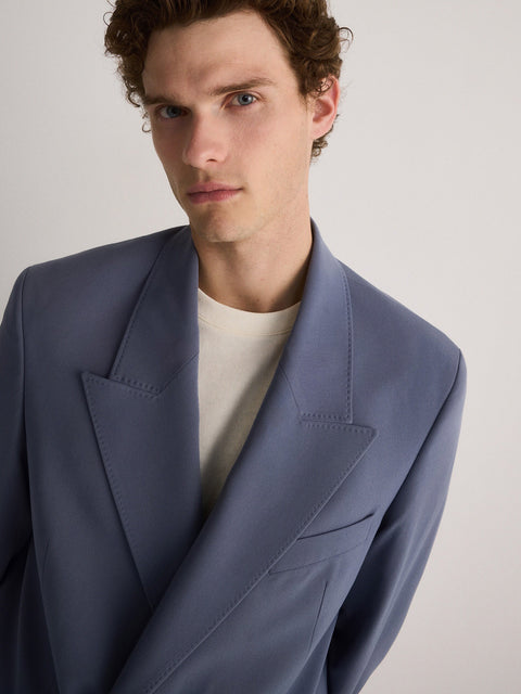 Man wearing a light blue blazer over a white shirt on a plain background