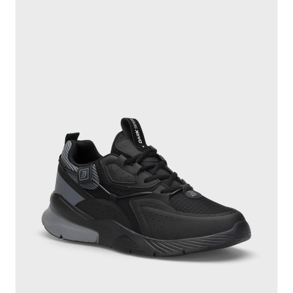 A black athletic sneaker with textured mesh panels, black laces, a black and gray midsole, and a black pull tab with white branding, shown on a light gray background.