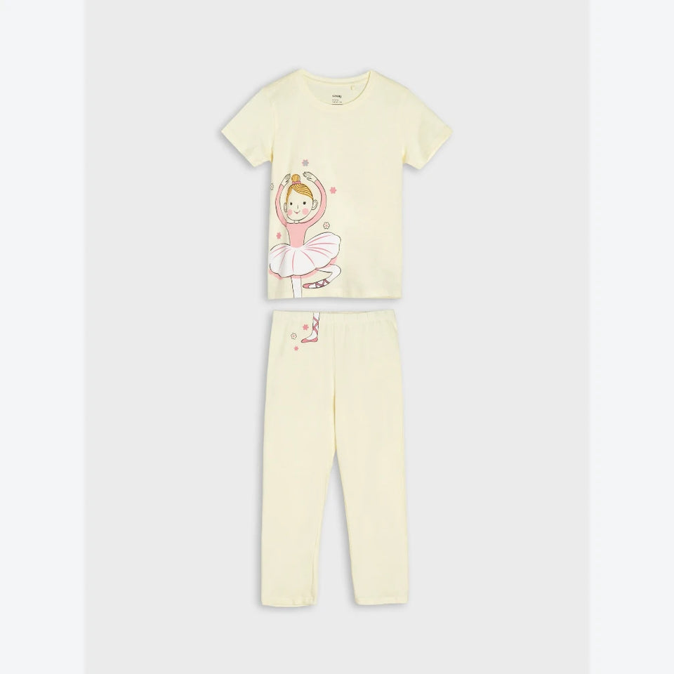 A two-piece children's pajama set in pale cream yellow, featuring a short-sleeve t-shirt with a cartoon ballerina graphic and matching long pants.