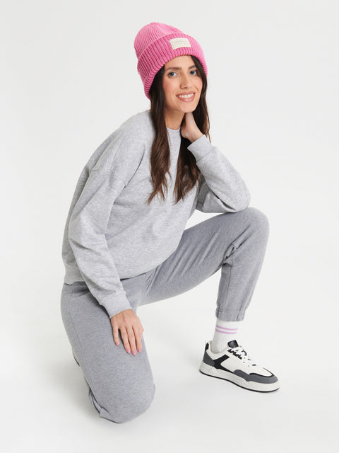 Woman wearing a gray tracksuit and pink beanie on a white background