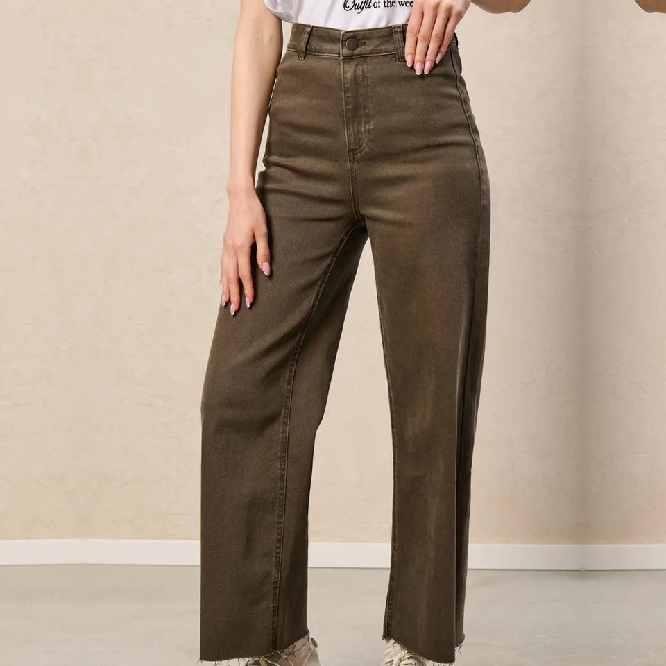 A person wearing high-waisted, wide-leg brown pants with a white graphic t-shirt, standing against a neutral beige wall.