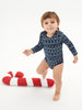 Child in a navy blue patterned onesie standing next to a red and white striped candy cane on a white background