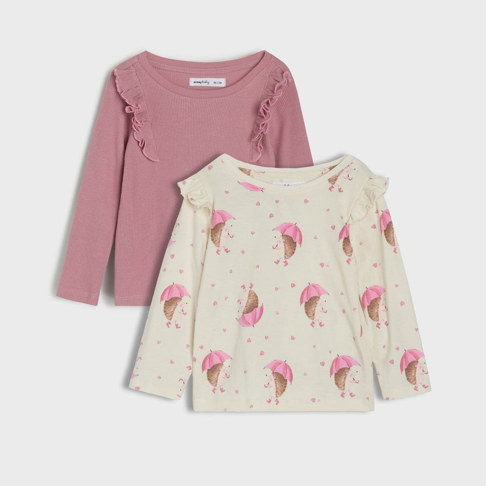 Two long-sleeve girls' tops layered together on a light gray background. The top behind is dusty pink with ruffle trim at the shoulders.