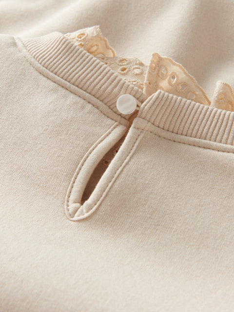 Close-up of a beige garment with a button and lace trim on a matching fabric background